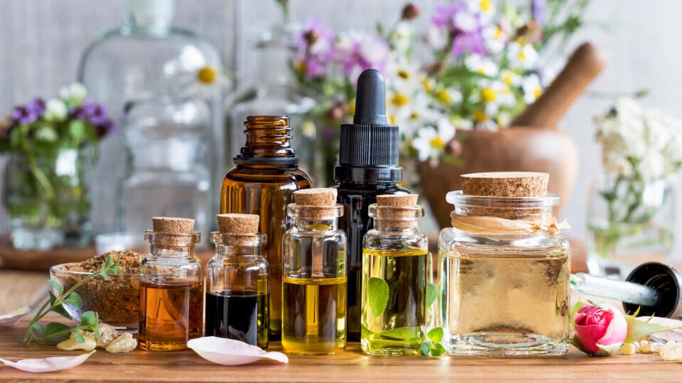 Selection of essential oils, with herbs and flowers in the background