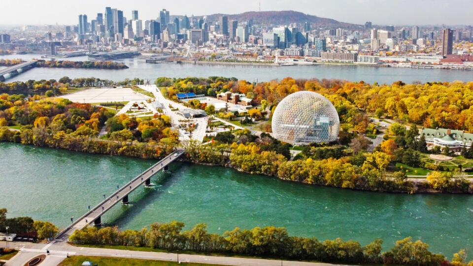 Pohľad na Montreal s okrúhlou budovou The Biosphere na ostrove Sv. Heleny na rieke rieky Sv. Vavrinca. Za mestskou štvrťou Villa-Marie sú postavené moderné mrakodrapy s vrchom Mount Royal v pozadí.