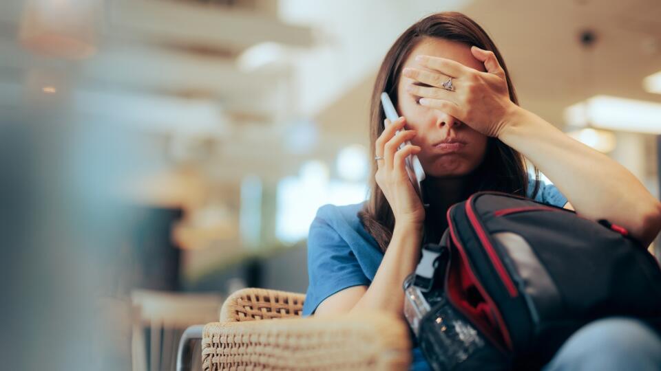 Unhappy,Woman,Talking,On,The,Phone,Waiting,In,An,Airport