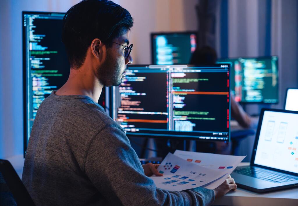Asian,Software,Developers,Working,On,Multiple,Screens,Displaying,Code,And