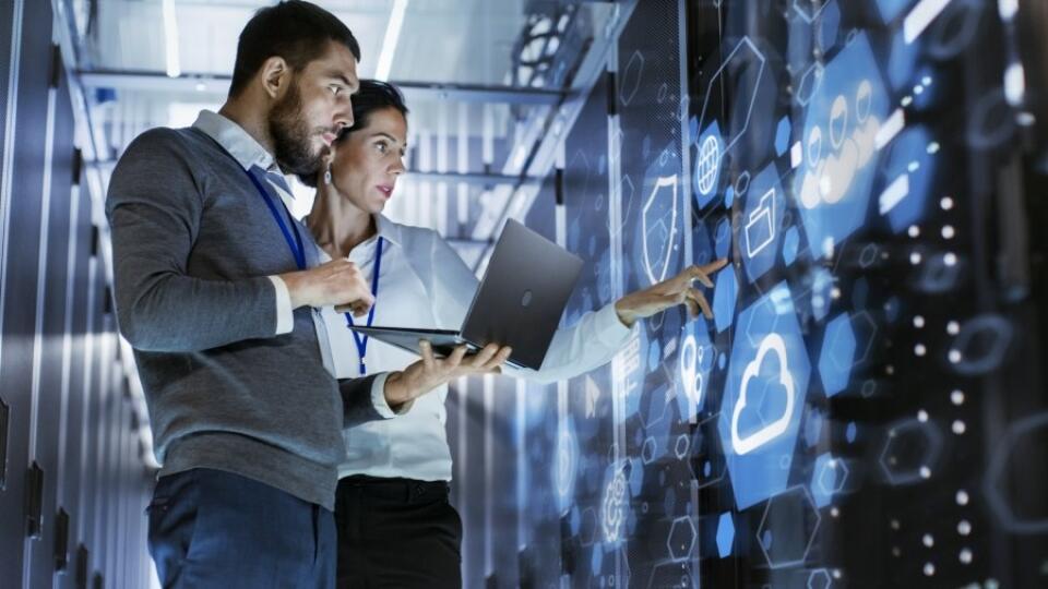 Male IT Specialist Holds Laptop and Discusses Work with Female Server Technician. They're Standing in Data Center, Rack Server Cabinet with Cloud Server Icon and Visualization.; Shutterstock ID 1062915392; Purchase Order: 4503738000; Job: ; Client/Licensee: Global Brand; Other: