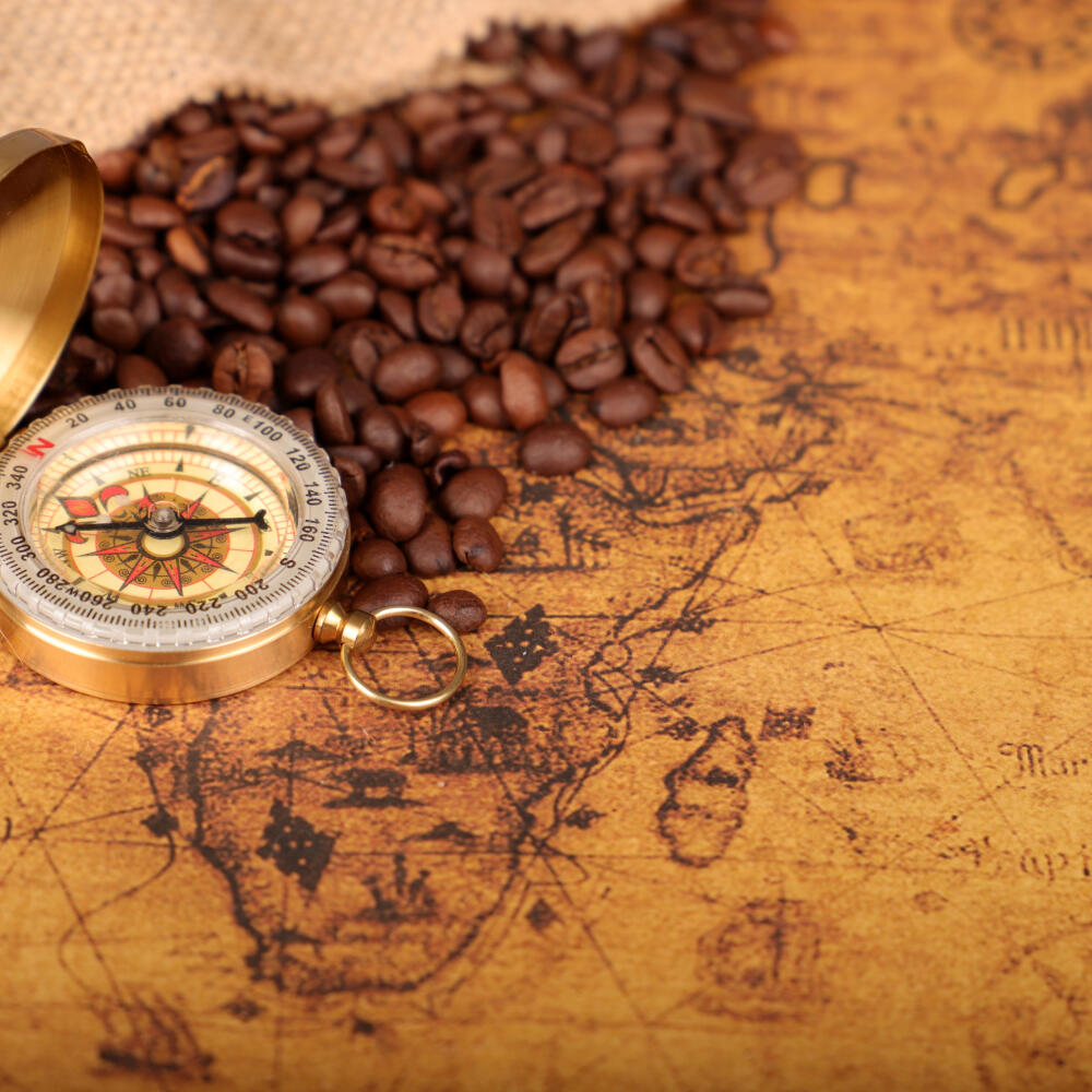 Coffee Beans and Vintage compass on an old world map - trade and explorer concept