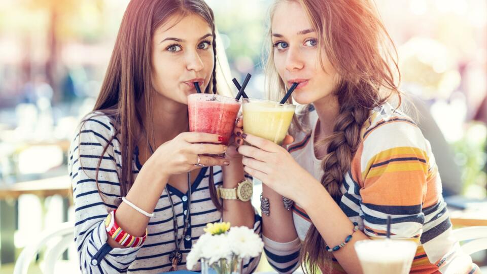 Teenage girls sitting together on street café, relaxing and enjoying cold smoothies
