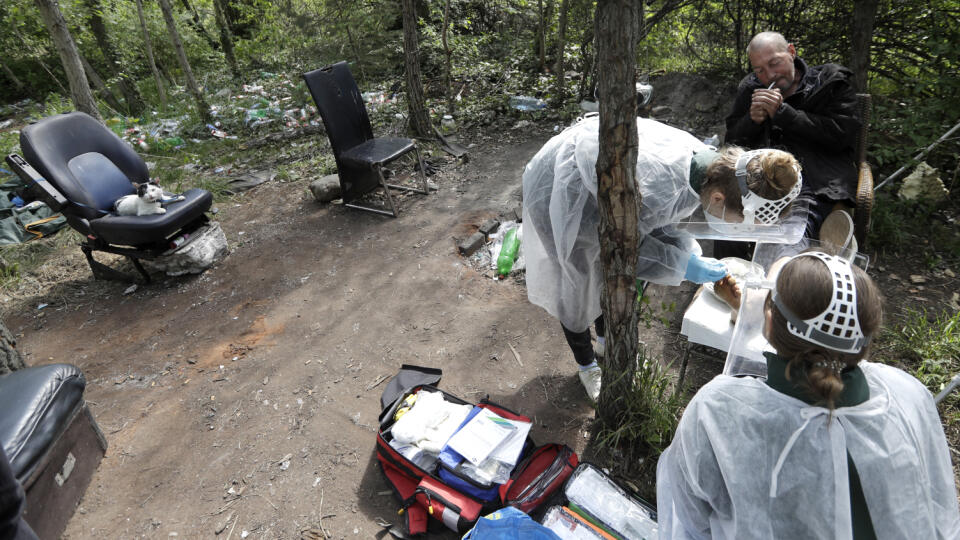 WA 23 Praha - Študentky medicíny v ochranných odevoch a štítoch ošetrujú bezdomovcovi zranenie nohy v Prahe vo štvrtok 30. apríla 2020. Napriek rizikám koronavírusovej pandémie skupina s názvom