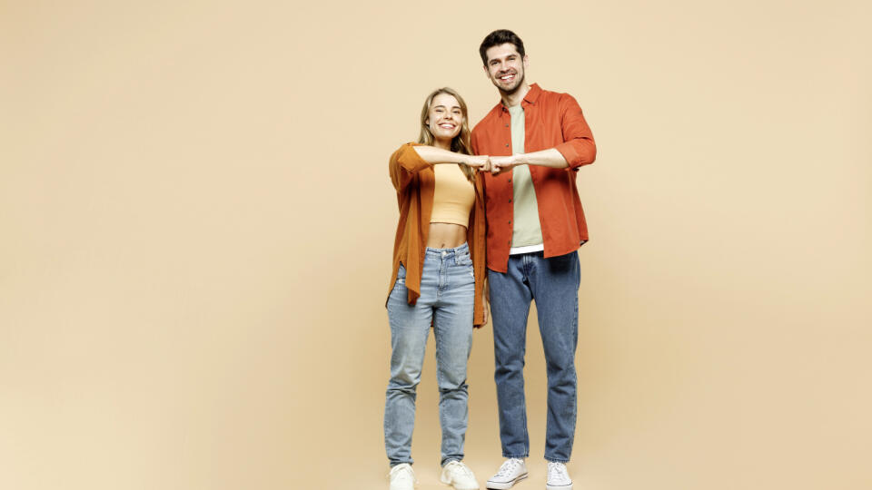 Full body smiling cheerful fun young couple two friends family man woman wear casual clothes together giving fist bump look camera isolated on pastel plain light beige color background studio portrait