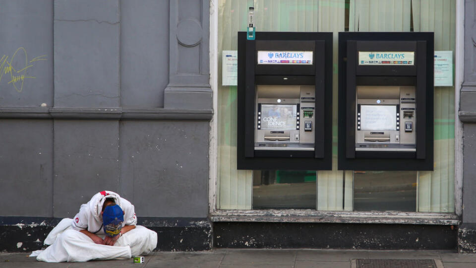A homeless person sits near Barclays Bank cash machine in