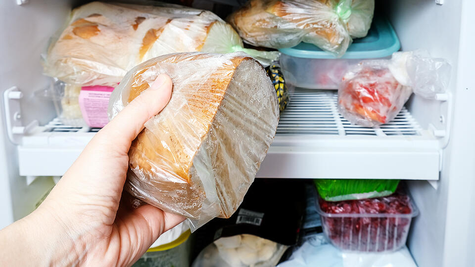 A hand putting a package of brown bread in reserve on a shelf of a home freezer, long life food storage concept