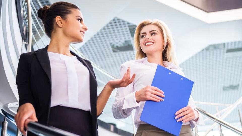 Two attractive bussiness women moving down the stairs and talking.