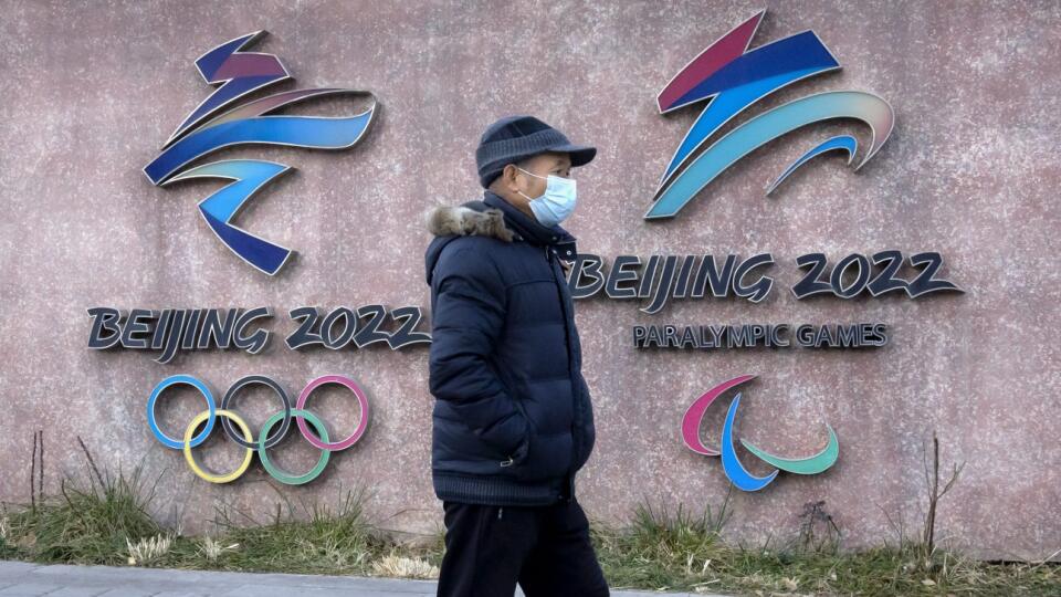 WA 38 Peking - Muž s ochranným rúškom na tvári kráča okolo loga zimných olympijských a paralampijských hier pred sídlom organizačného výboru hier v Pekingu vo štvrtok 16. decembra 2021. Organizátori zimných olympijských hier v Pekingu sprísnili bezpečnostné opatrenia súvisiace s pandémiou koronavírusu. Športovci si podľa nich musia ponechať v
