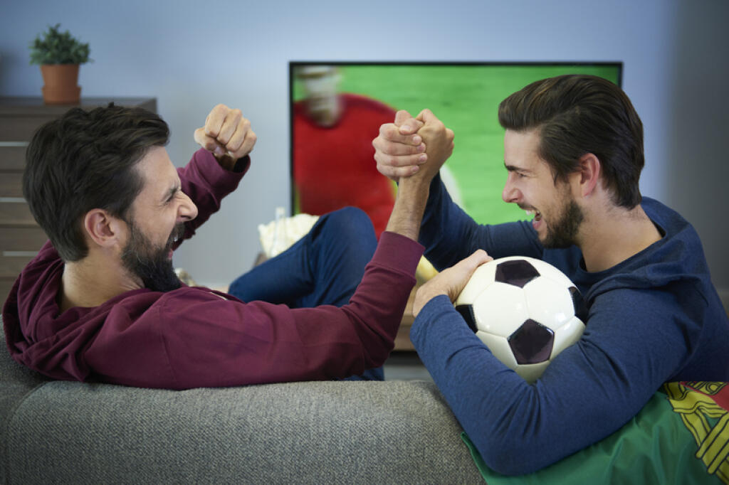 Two football fans watching Tv and cheering