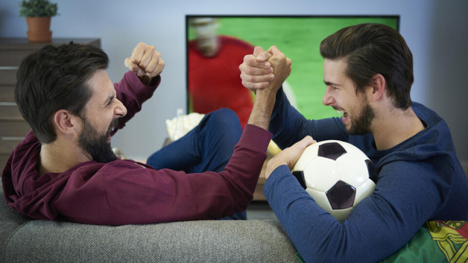 Two football fans watching Tv and cheering