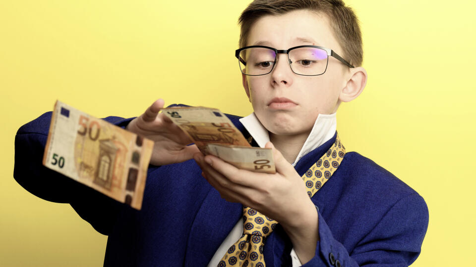 The child scatters money, a boy in a suit throws euros, a portrait of a child on a yellow background. new