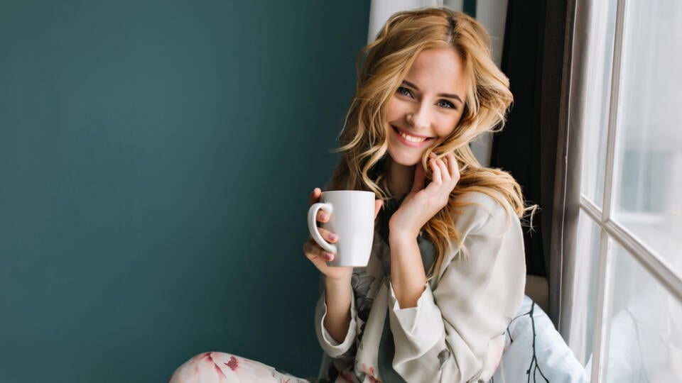 Cheerful,Blonde,Woman,Relaxing,And,Sitting,On,Window,Sill,,Holding