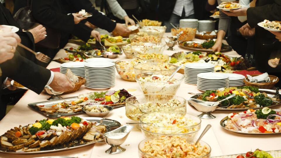 Catering table full of tasty food. Many hands of unrecognizable persons.