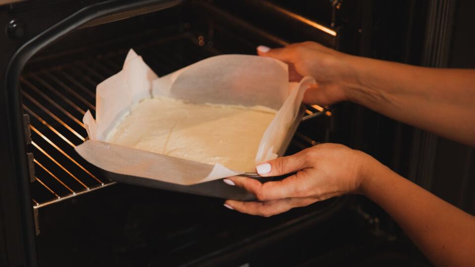Female hands put in the oven a baking dish with a batter cake.
