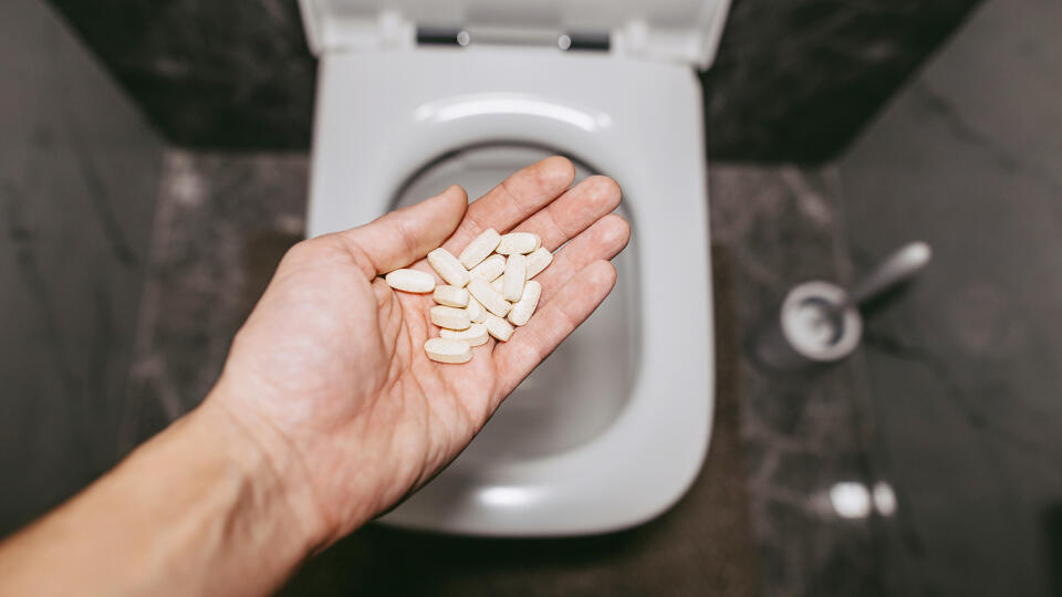 A hand throws pills into the toilet for flushing water