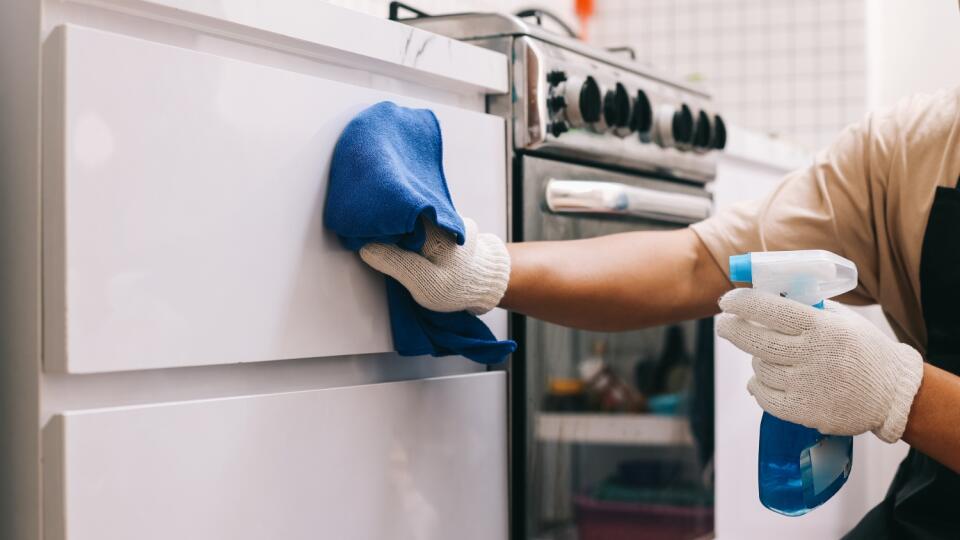 Closeup of hands cleaning kitchen cabinets with detergent spray bottle and cloth