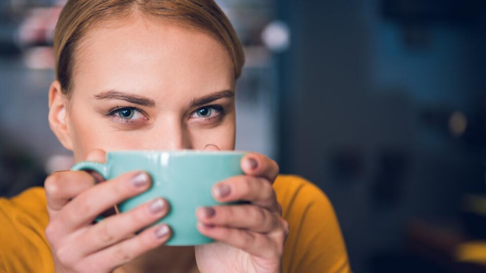 Cheerful girl keeping mug near mouth