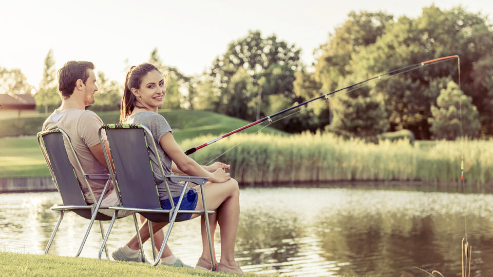 Back view of beautiful couple catching fish in the pond using a fishing rod. Girl is looking at camera and smiling