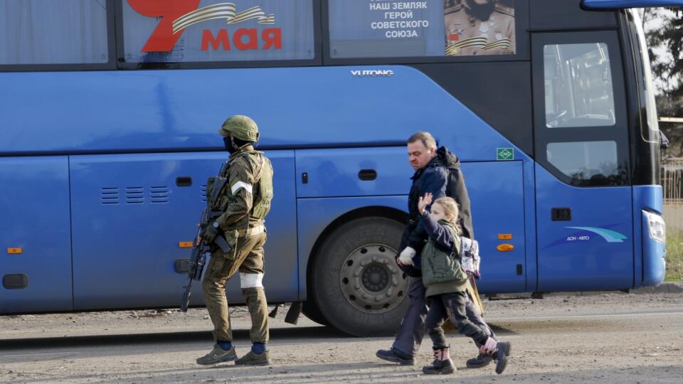 Muž a dievča, ktorí sa skrývali v oceliarňach Azovstaľ, kráčajú k autobusu s nápisom 9. máj, ktorý stráži ruský vojak v obliehanom ukrajinskom prístavnom meste Mariupol počas 72. dňa ruskej invázie na Ukrajinu v piatok 6. mája 2022.