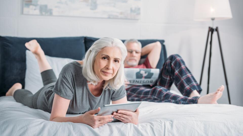 woman using tablet while husband reading newspaper in bed