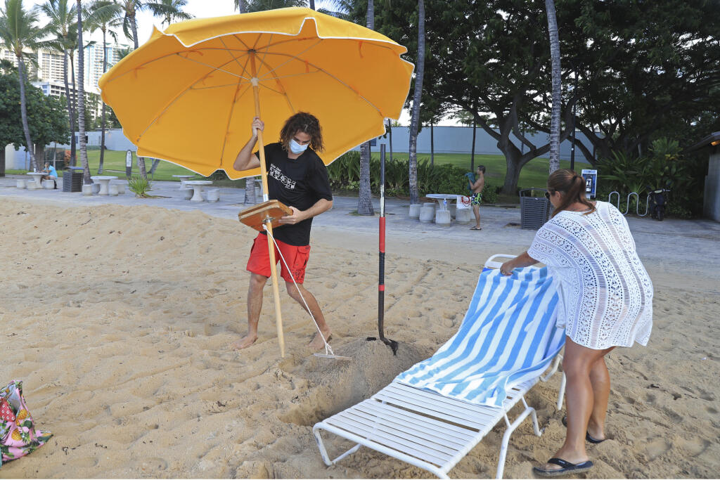 KK35 Honolulu - Na snímke návštevníčka na pláži Waikiki na Honolulu 15. októbra 2020. Nový cestovateľský testovací program umožní návštevníkom, ktorí majú negatívny test na COVID-19, prísť na Havaj a vyhnú sa dvojtýždňovej povinnej karanténe, ktorá začala platiť vo štvrtok 15. októbra. Pandémia nového koronavírusu spôsobila ničivý pokles v havajskej ekonomike založenej na cestovnom ruchu. FOTO TASR/AP
Mitch Kemp, left, a worker at a Waikiki Beach rental company, sets up an umbrella for visitor L