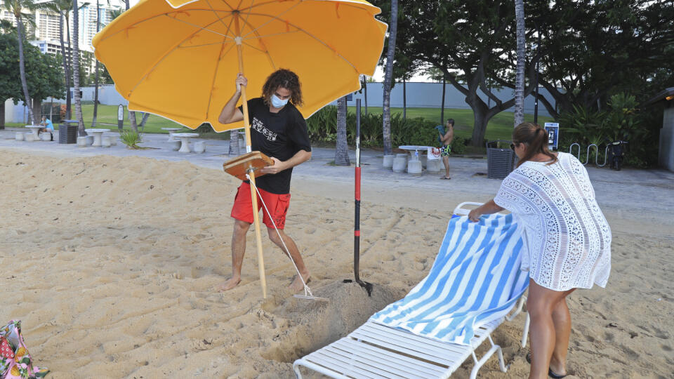 KK35 Honolulu - Na snímke návštevníčka na pláži Waikiki na Honolulu 15. októbra 2020. Nový cestovateľský testovací program umožní návštevníkom, ktorí majú negatívny test na COVID-19, prísť na Havaj a vyhnú sa dvojtýždňovej povinnej karanténe, ktorá začala platiť vo štvrtok 15. októbra. Pandémia nového koronavírusu spôsobila ničivý pokles v havajskej ekonomike založenej na cestovnom ruchu. FOTO TASR/AP
Mitch Kemp, left, a worker at a Waikiki Beach rental company, sets up an umbrella for visitor L