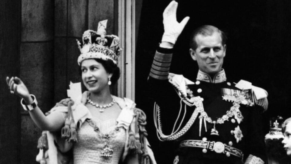 Queen Elizabeth II wearing the Imperial State Crown and the Duke of Edinburgh in uniform of Admiral of the Fleet wave from the balcony to the onlooking crowds around the gates of Buckingham Palace after the Coronation.