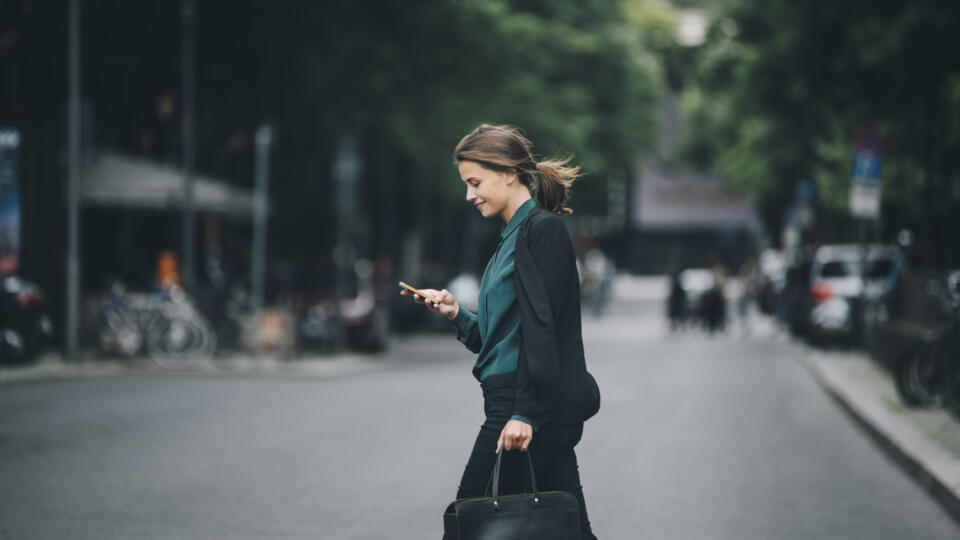 Confident businesswoman using smart phone while crossing street in city