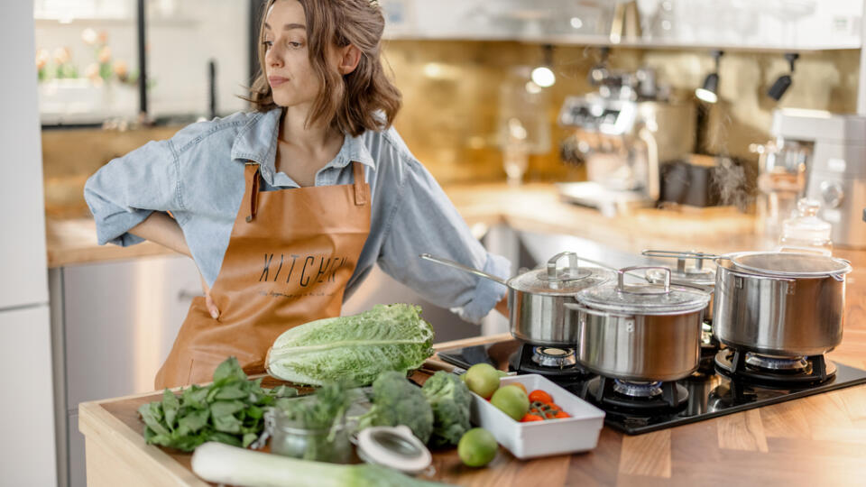 Woman,Staying,Near,Cooker,With,Pans,And,Green,Ingredients,On