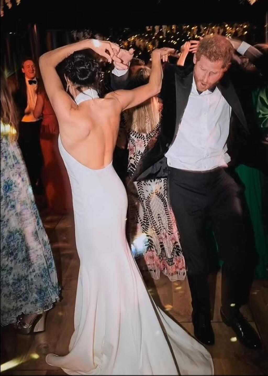Namiesto honosných šiat má Meghan na záberoch jednoduché biele dlhé šaty s odhalenými ramenami a hlbokým výstrihom na chrbte.