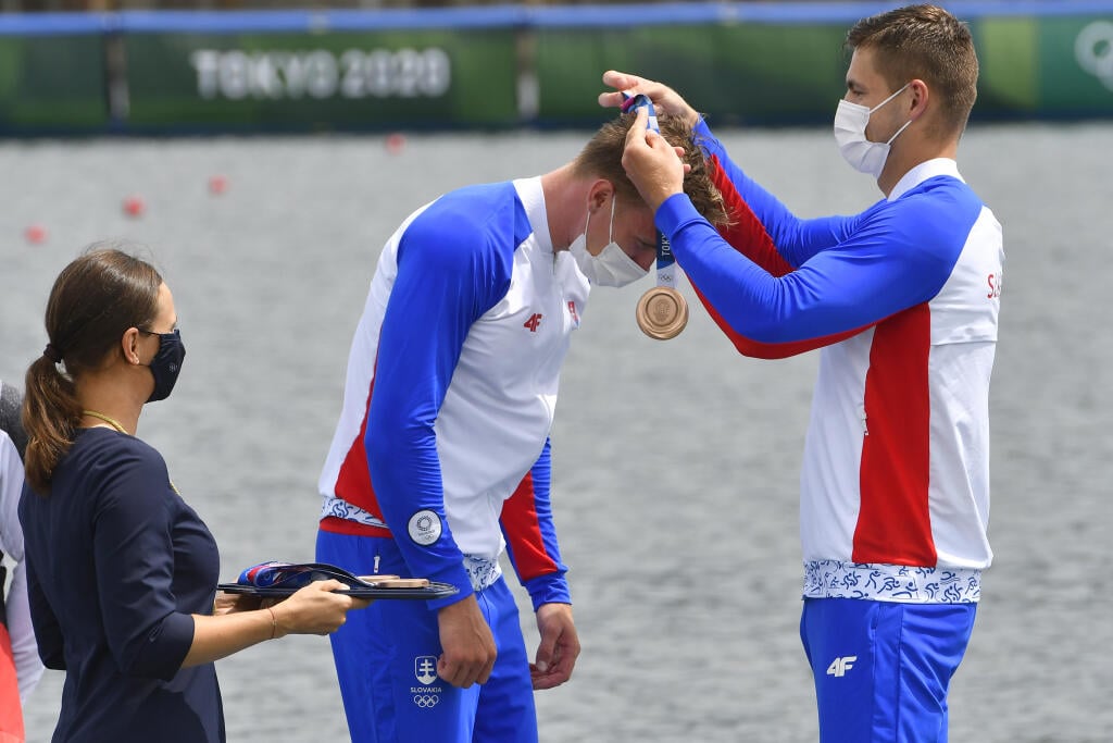 Na snímke slovenská posádka rýchlostných kanoistov K4 v zložení Samuel Baláž, Denis Myšák, Erik Vlček a Adam Botek získala bronzovú medailu na 500 metrov počas XXXII. letných olympijských hier v Tokiu, 7. augusta 2021. Na snímke Denis Myšák dekoruje Samuela Baláža bronzovou medailou, ktorú im priniesla Danka Barteková (vľavo) počas medailového ceremoniálu. FOTO TASR - Michal Svítok