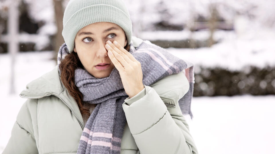 Young woman having itching eyes health problem. Sick woman in winter snow touching her sensitive eye