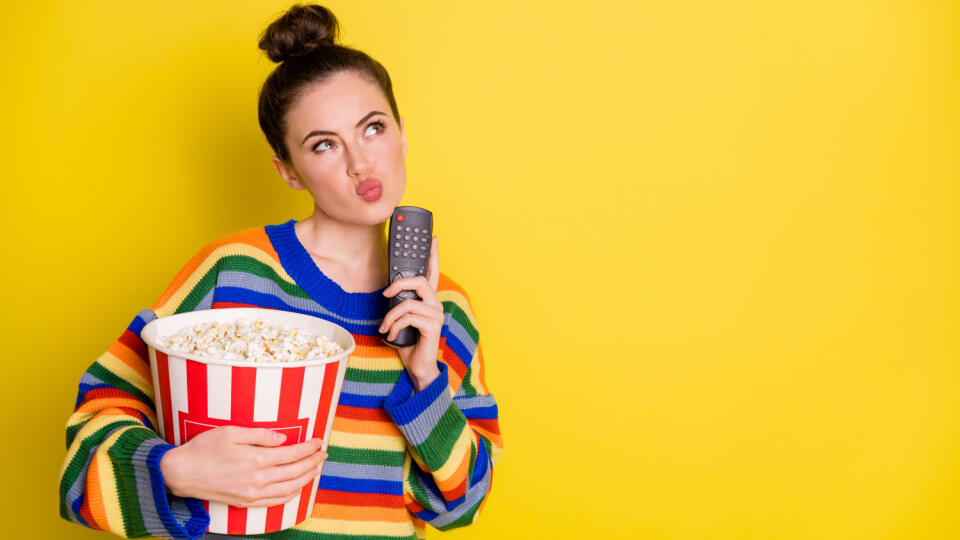 Photo of young attractive woman think hold remote control eat pop-corn look empty space isolated over yellow color background