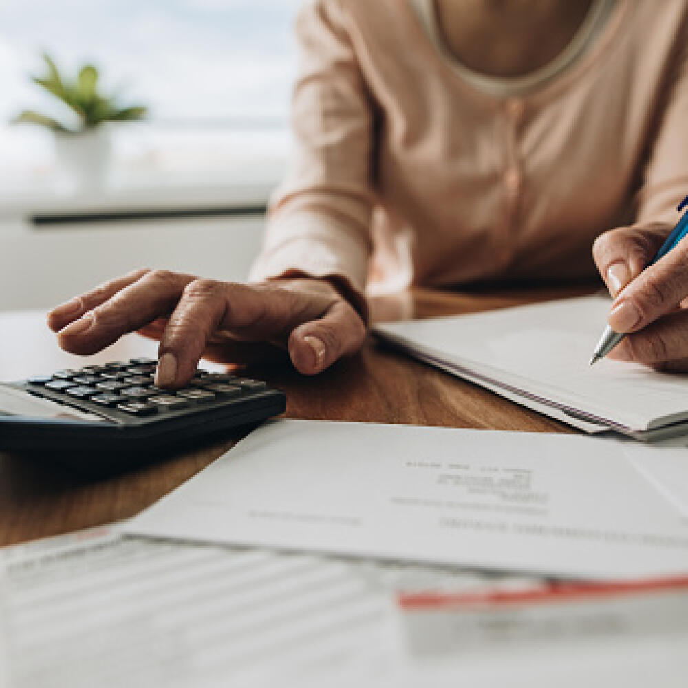 Close up of unrecognizable woman using calculator while going through bills and home finances.