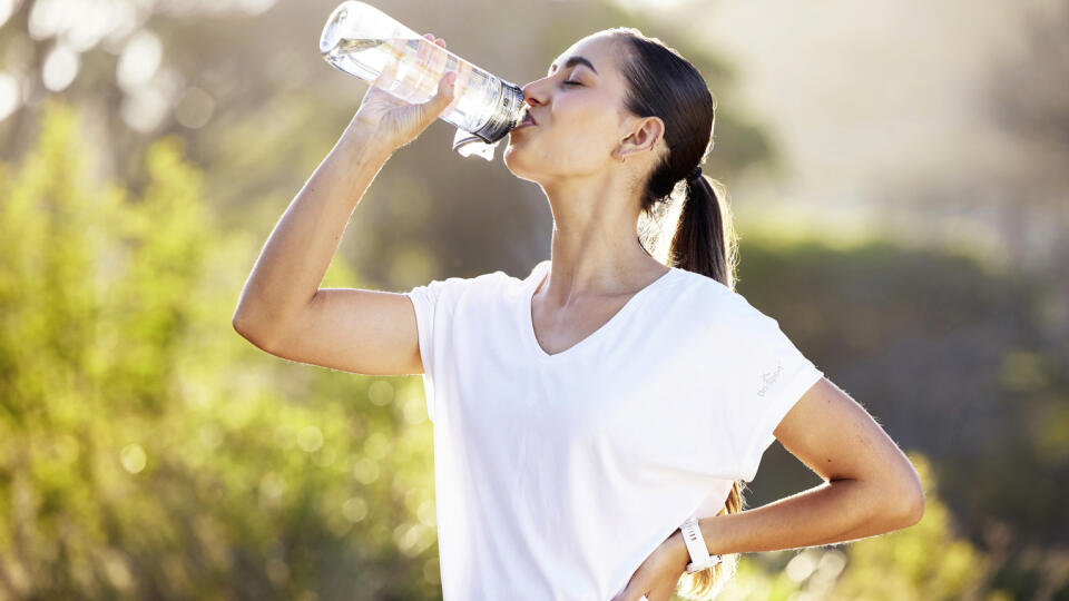 Drinking water, fitness and exercise woman after sports run and training in nature. Workout, hiking and walking challenge with a bottle of a female runner in summer ready for running for health