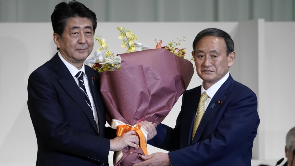 Na snímke vľavo japonský premiér Šinzó Abe a nový premiér Jošide Suga pózujú s kyticou kvetov v Tokiu 14. septembra 2020.