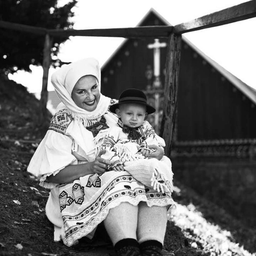 Mamička so synčekom v sviatočnom kroji. Dieťa spokojne sedí na rukách matky, nôžky má zabalené vo vlnenom obrúsku. Je zvláštne, že matka má na nohách hrubé pletené pančuchy a šatku zaviazanú