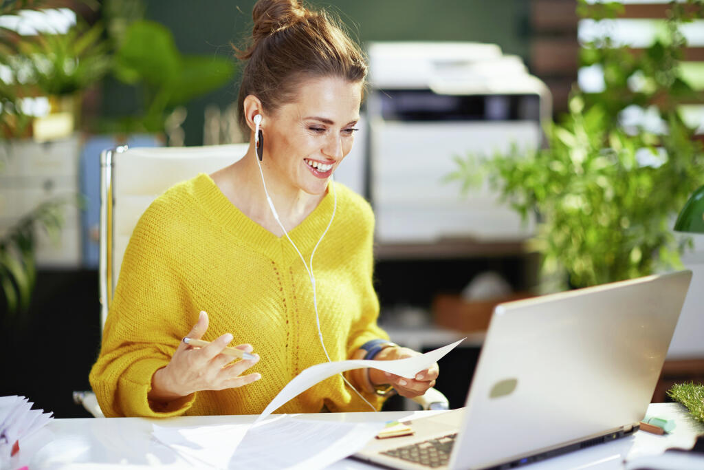 smiling elegant small business owner woman in yellow sweater with laptop having virtual meeting in the modern green office.