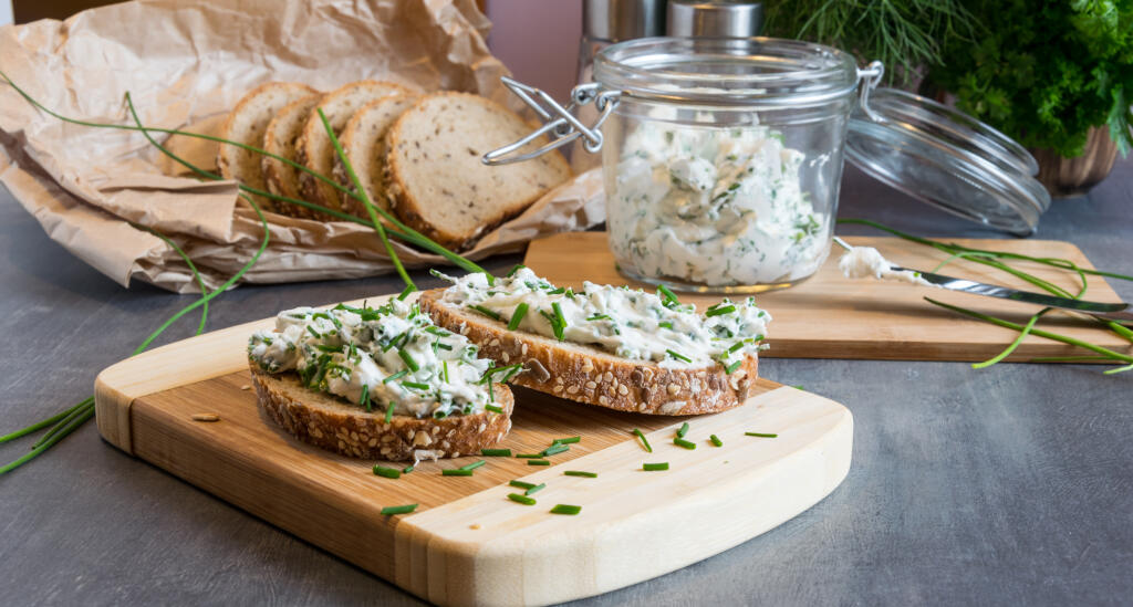 Home made bread on a wooden cutting board with curd cheese and ricotta and herbs. Decorated with green herbs