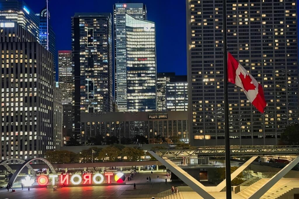 Toronto, Canada - 24 October 2022: a pole with the canadian national flag in front of city hall with view of skyscrapers at night in the city