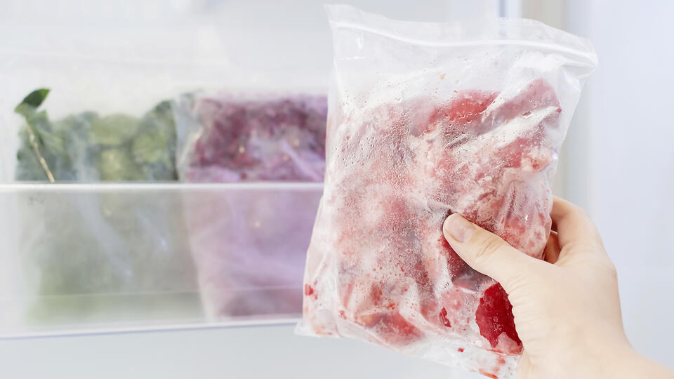 Female hand holds plastic bag with a zip fastener with frozen strawberries against the background of an open freezer with other vegetables.