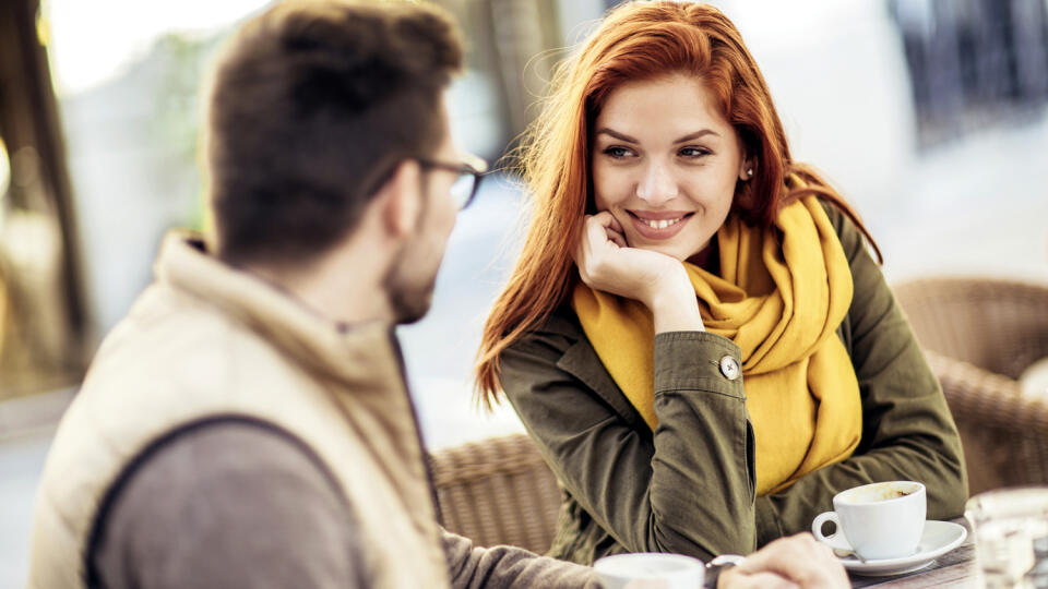 Attractive young couple in love sitting at the cafe table outdoors, drinking coffee