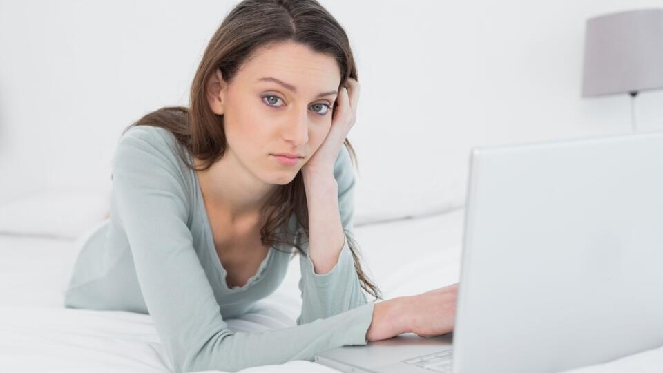 Casual sad young woman using laptop in bed