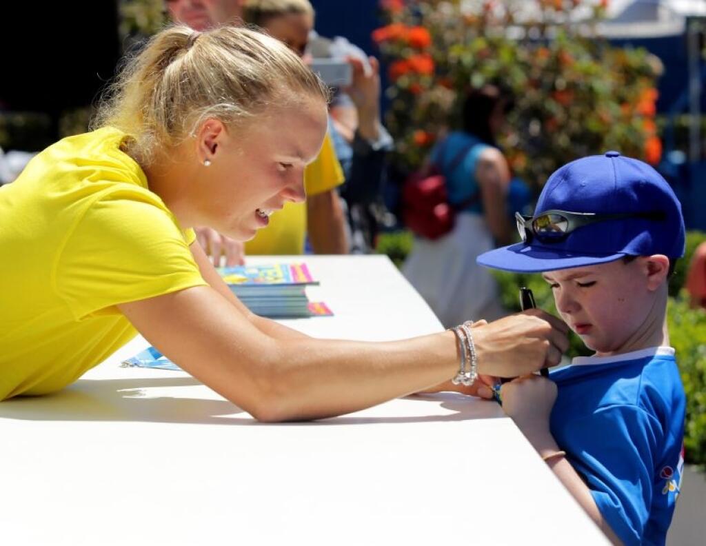 In this photo released by Tennis Australia, Denmark's Caroline Wozniacki signs her autograph onto the shirt of a young fan at the Australian Open tennis championship in Melbourne, Australia, Monday, Jan. 13, 2014. (AP Photo/Tennis Australia,Fiona Hamilton)