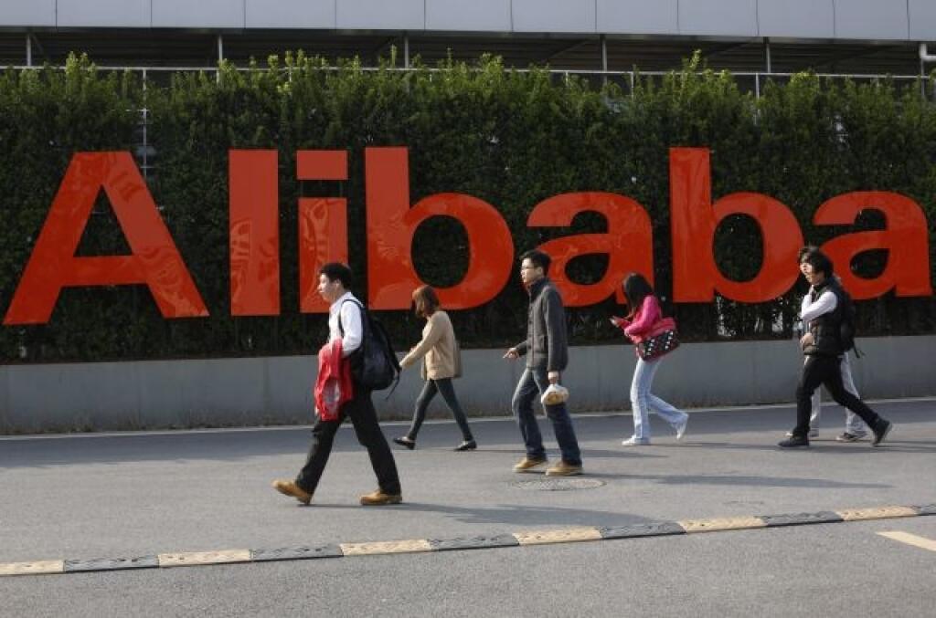 FILE - In this March 17, 2014 file photo, people walk past a company logo at the Alibaba Group headquarters in Hangzhou, in eastern China's Zhejiang province. Alibaba Group’s U.S. stock offering is a wakeup call about an emerging wave of technology giants in China’s state-dominated economy. Until now, Chinese companies that made a splash in global stock markets were state-owned banks and oil companies. But they are big by decree, not because they sell products customers want. By contrast, privat