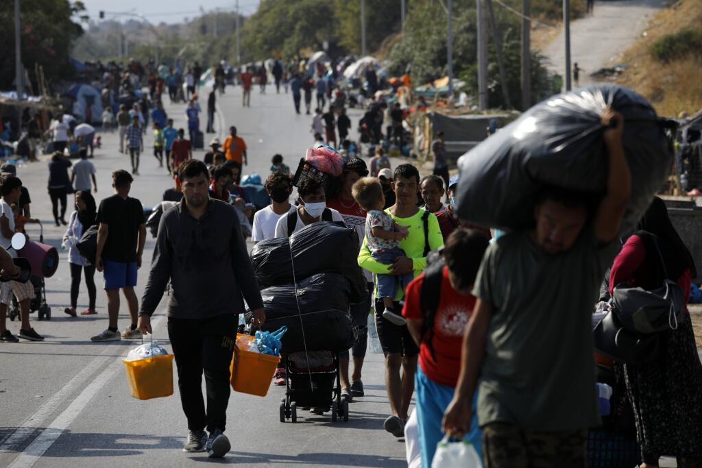 KK13 Lesbos - Migranti sa presúvajú so svojimi vecami z tábora Morie do mesta Mytilene na gréckom ostrove Lesbos 12. septembra 2020.  Grécka polícia ostrove Lesbos spustila vo štvrtok operáciu, ktorej cieľom je presťahovať stovky migrantov bez prístrešia do provizórneho stanového tábora. Ide o obyvateľov preľudneného tábora Moria, ktorý minulý týždeň zničil rozsiahly požiar. FOTO TASR/AP
Migrants carry their belongings as they flee a road leading from Moria to the capital of Mytilene, on the nor