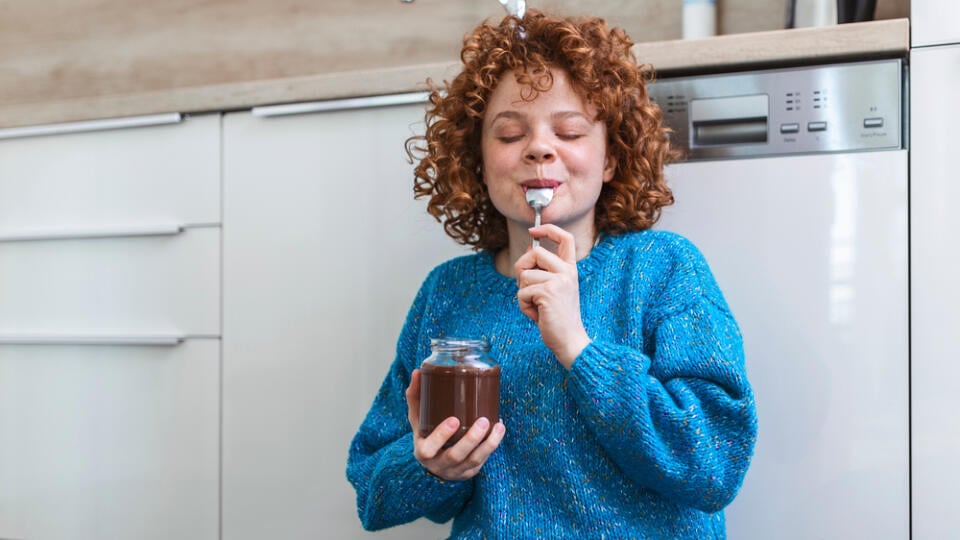 Young,Woman,Eating,Chocolate,From,A,Jar,While,Sitting,On