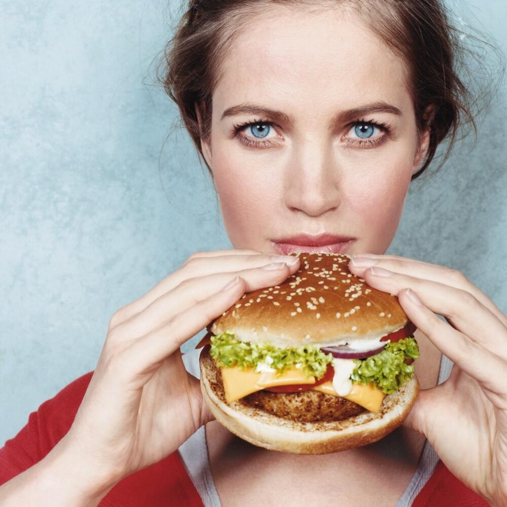 Frau mit blauen Augen hält Cheeseburger in den Händen