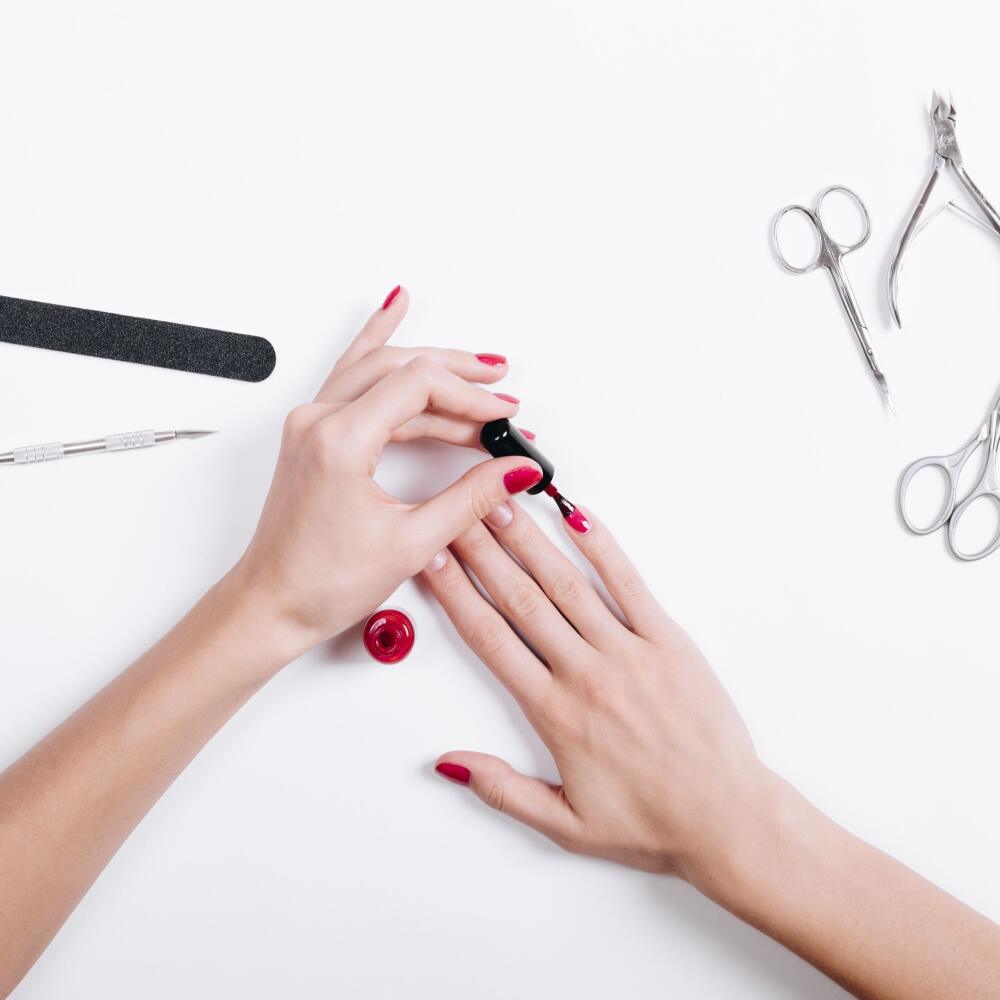 Top view of a woman's hands with red nail polish and manicure tools
